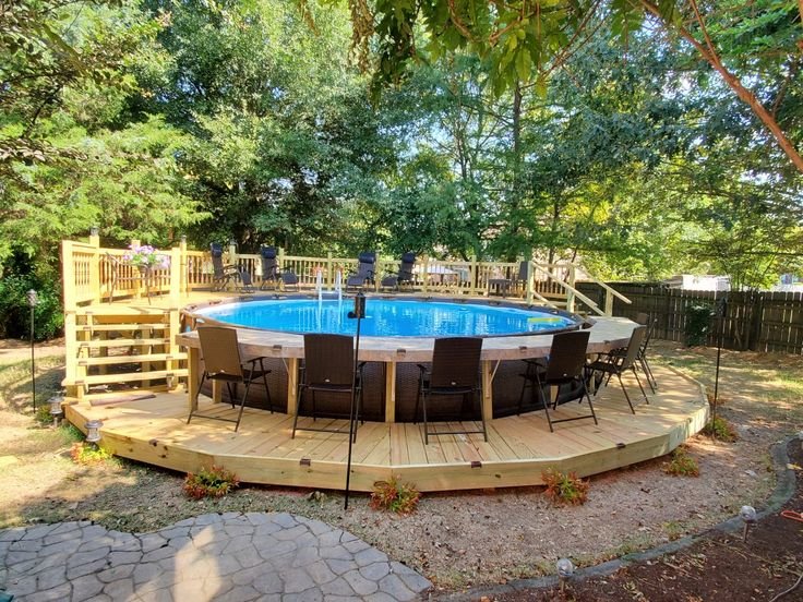 Above-ground pool with wooden deck and seating area surrounded by trees in a private backyard.